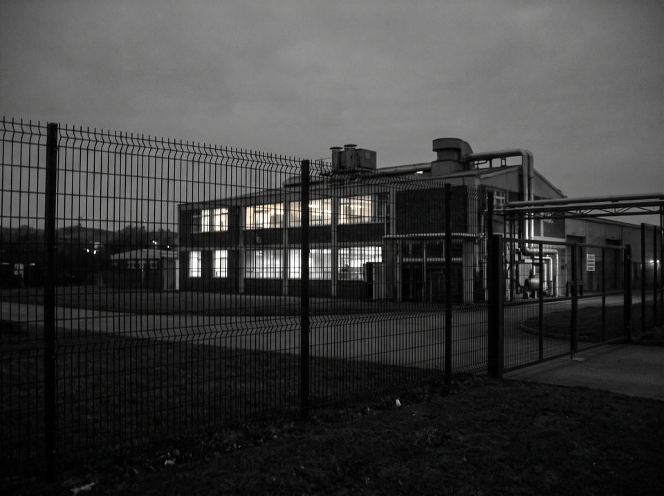 The Standardised Staples factory at dusk, lights on in a few windows